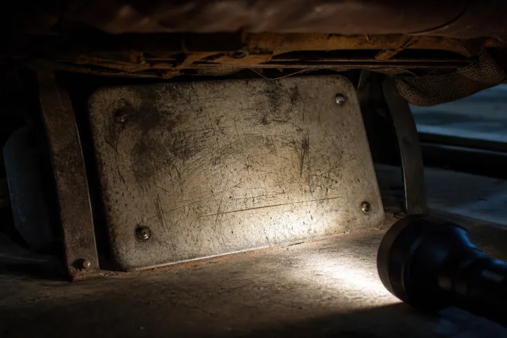 Dettaglio sotto un vecchio sedile d'auto con una piastra graffiata illuminata da una torcia