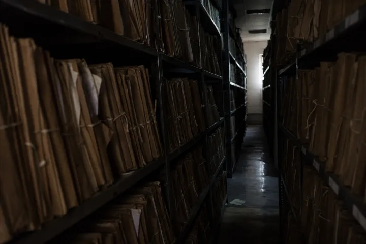 Corridoio d’archivio giudiziario con fascicoli sigillati e luce fredda