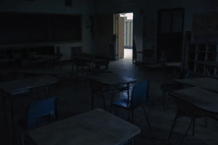 Un'aula vuota di notte con i banchi in disordine e una luce fredda dal corridoio