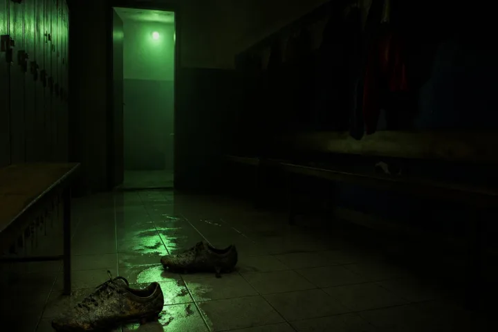 Spogliatoio buio con scarpe infangate e riflessi verdi sul pavimento
