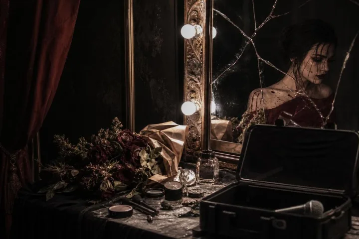 Camerino buio con specchio incrinato, fiori appassiti e custodia di microfono aperta